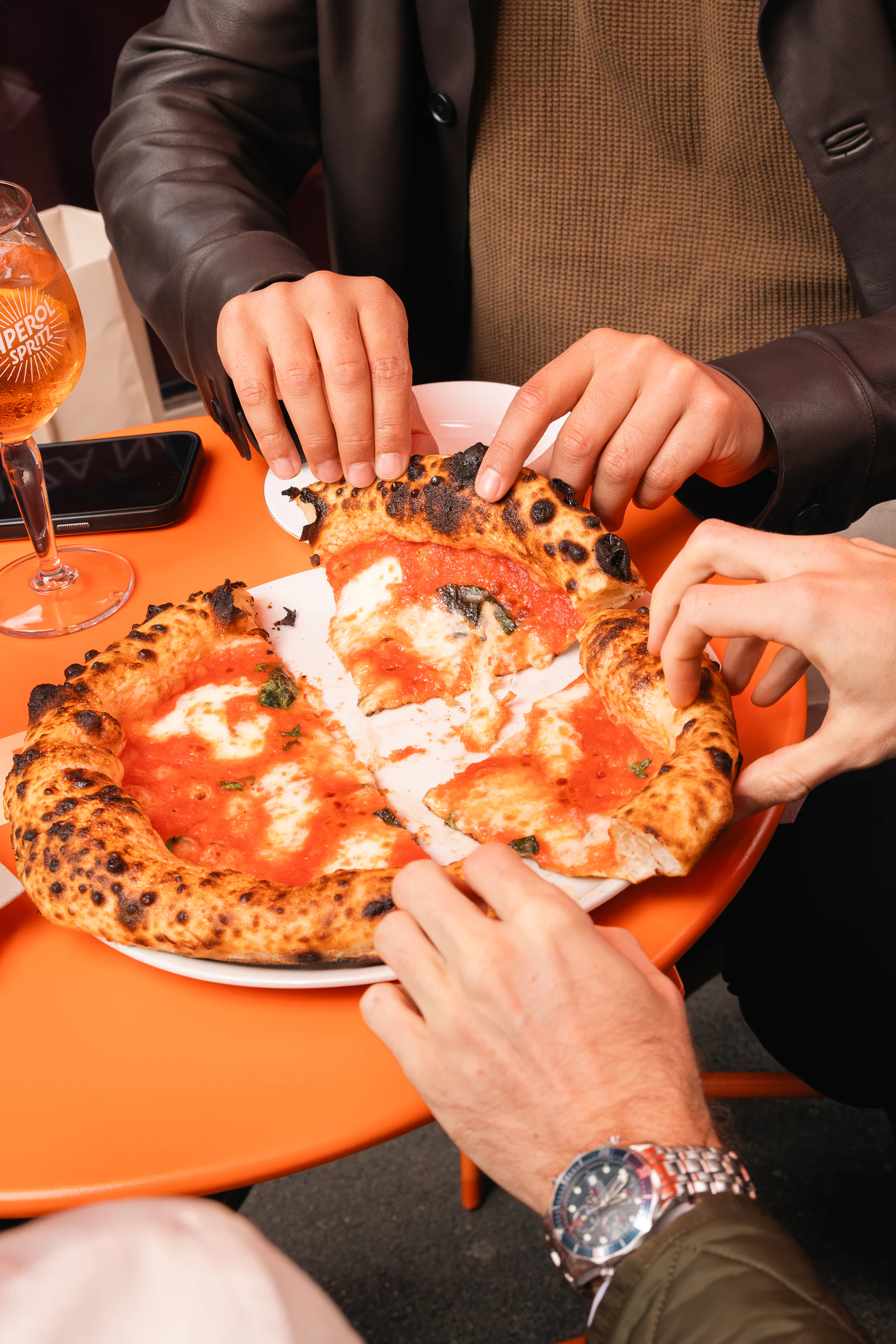 Hands reaching in to take slices from a shared pizza