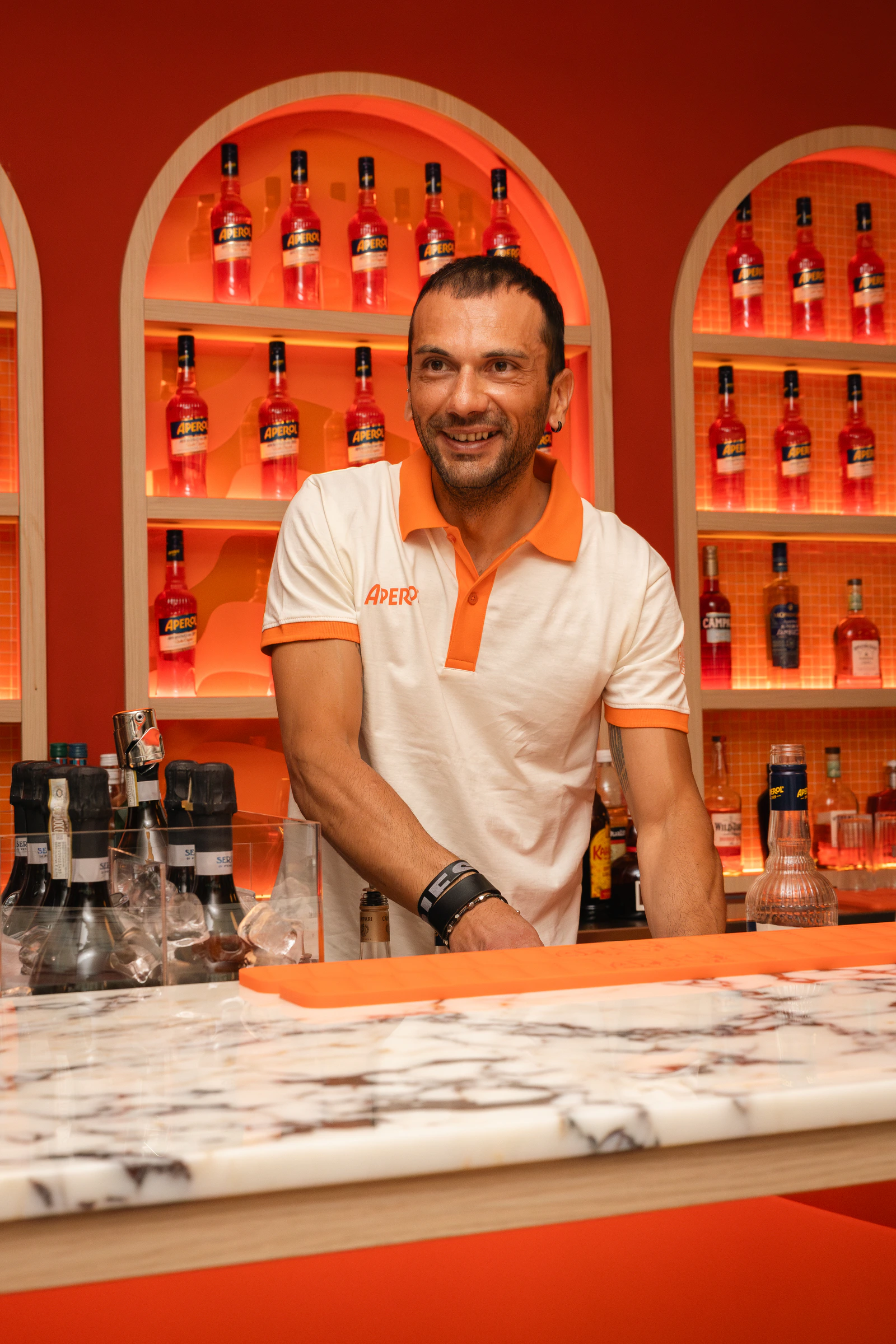 A bartender at the marble counter, the bottle wall behind him