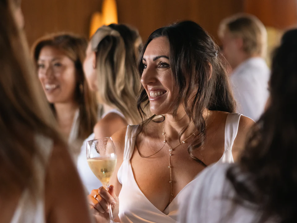 Guests in white laughing together on the terrace, wine glasses in hand