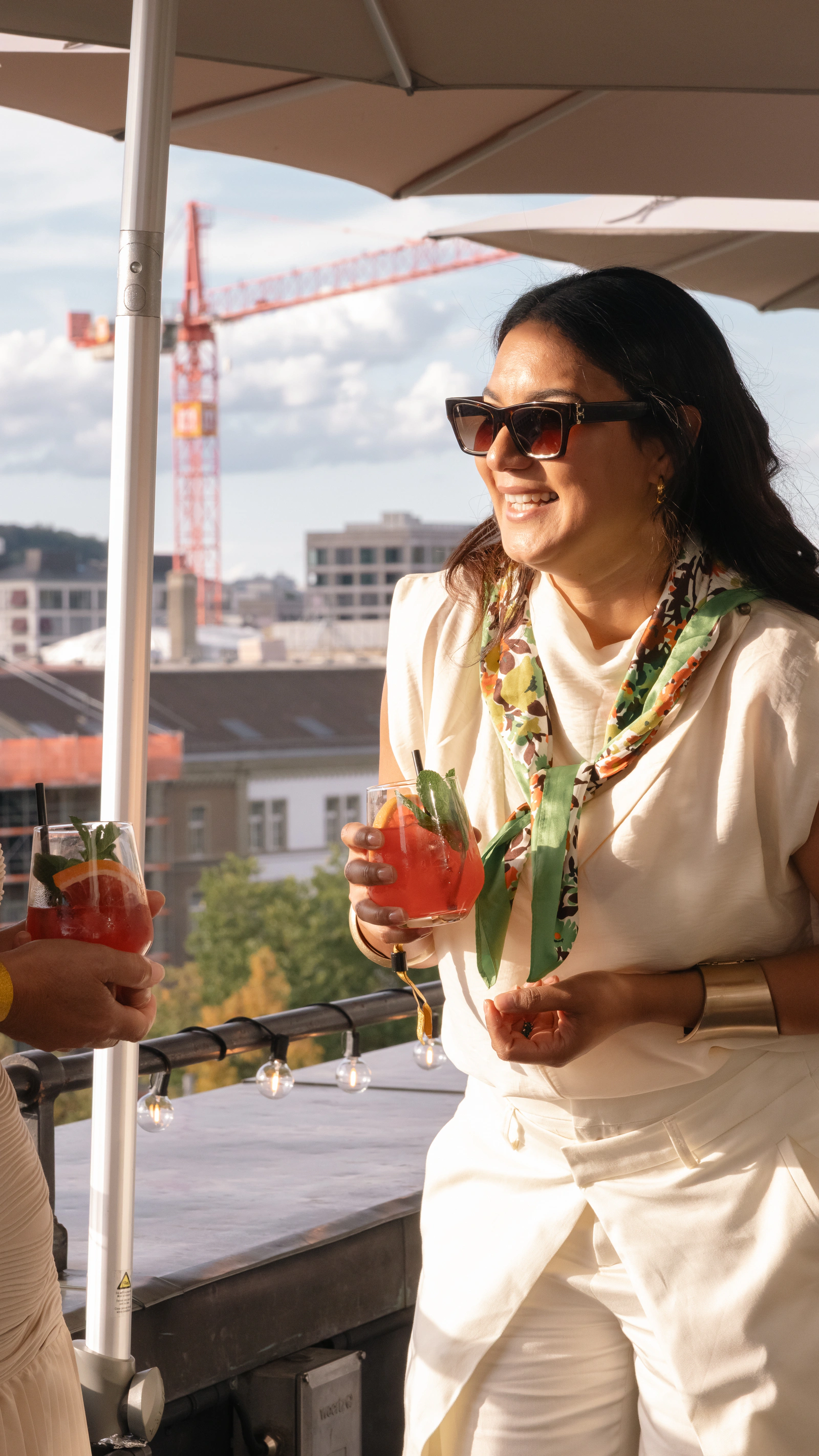 A guest in white and sunglasses on the terrace, rooftops and a crane behind her