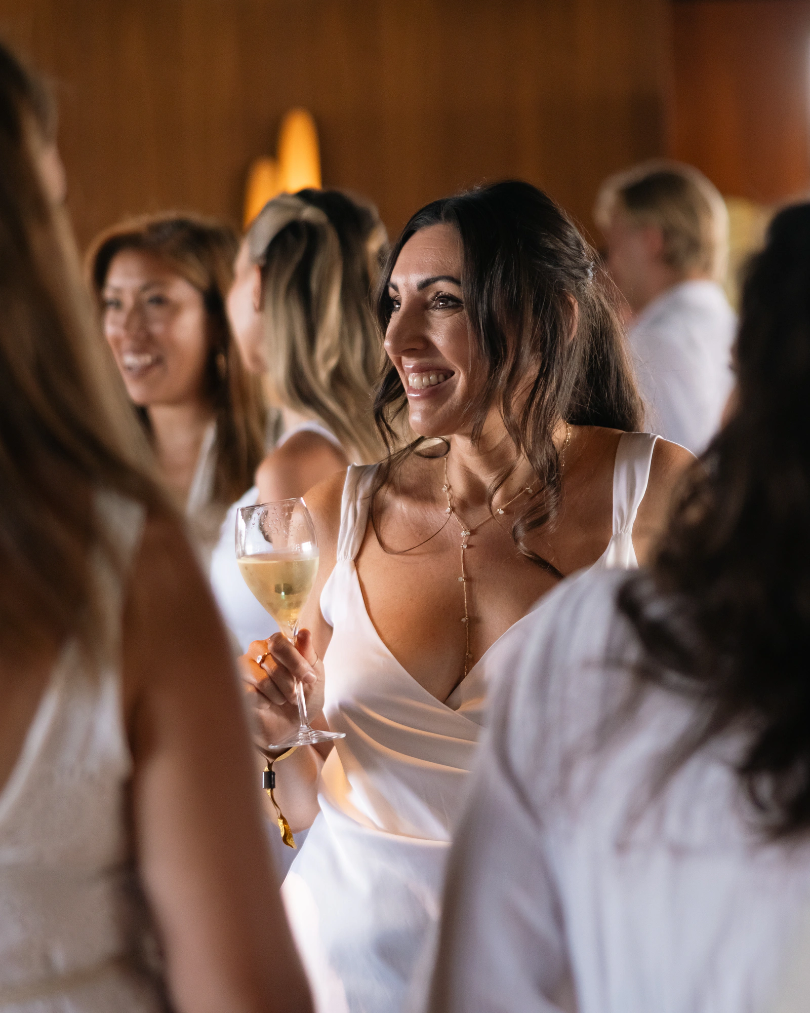 Guests in white laughing together on the terrace, wine glasses in hand