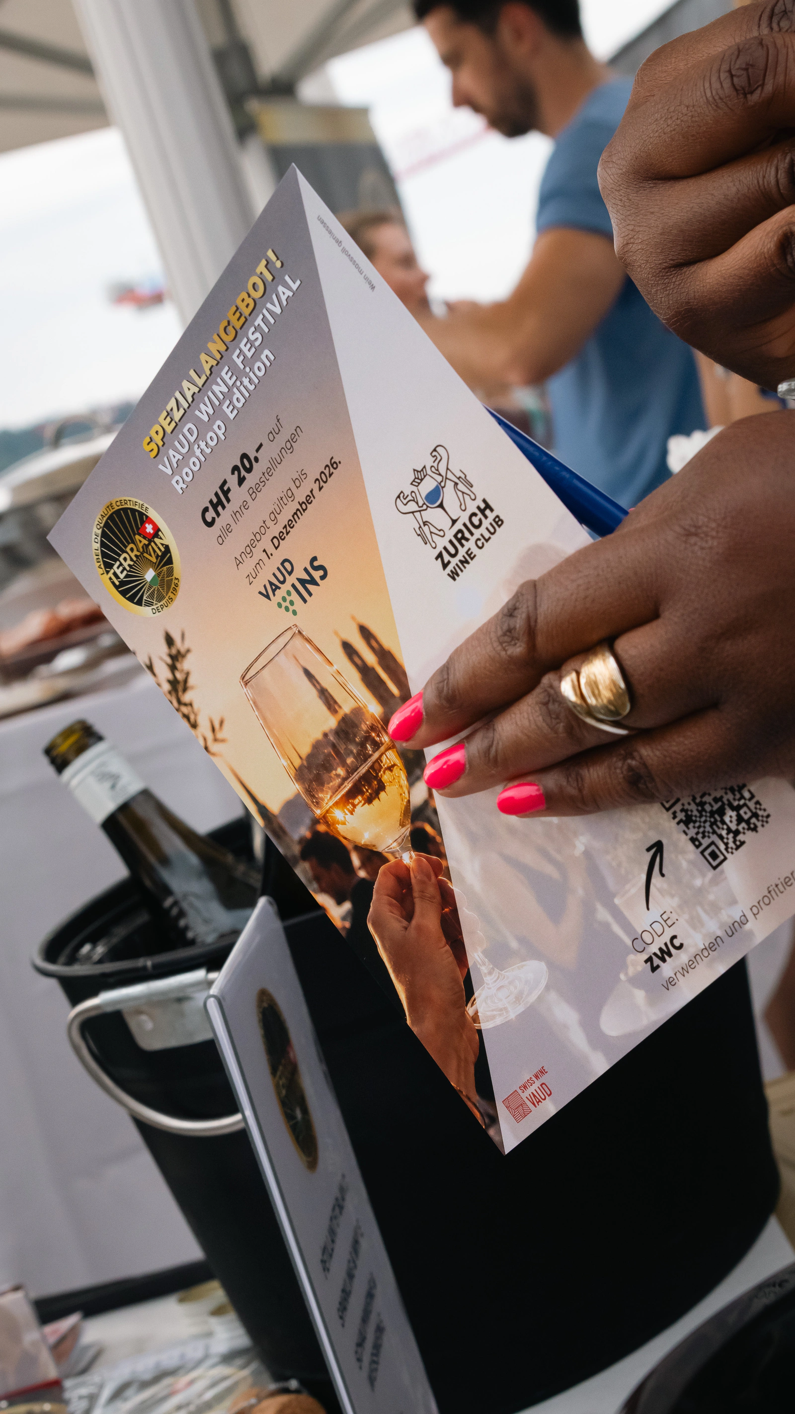 A hand holding the tasting programme over the bottles