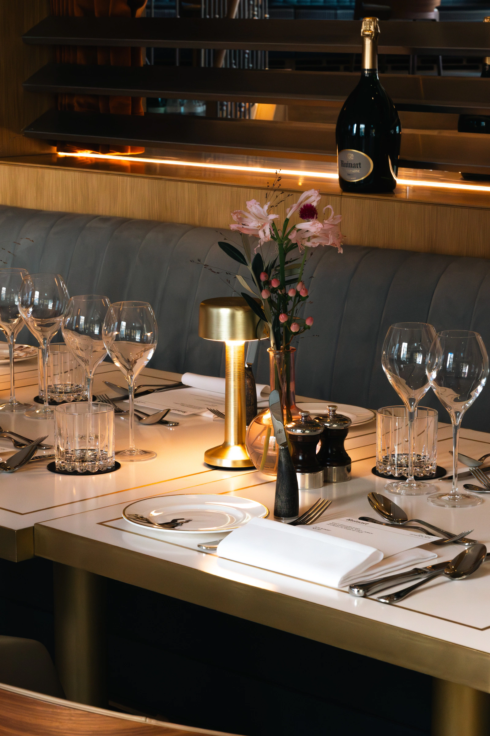 A banquette table laid with glassware and a small brass lamp